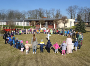 Duża grupa dzieci stoi w kole w ogrodzie przedszkolnym wokół kukły Marzanny.